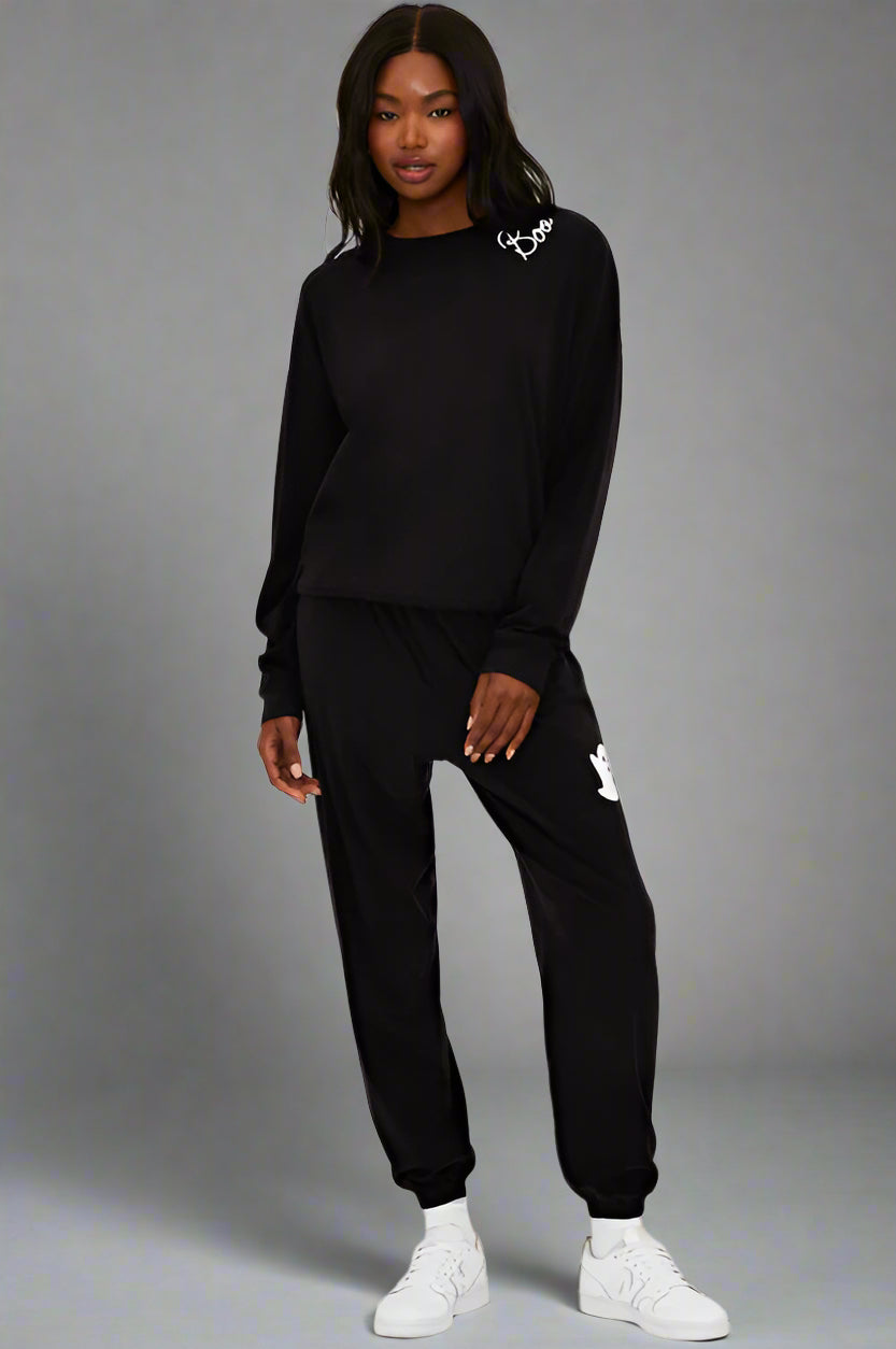Person wearing a black tracksuit with brand logos on a white background
