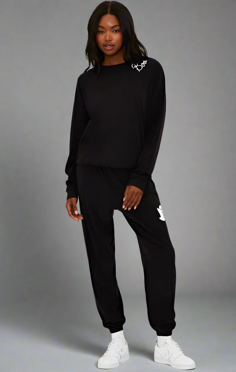 Person wearing a black tracksuit with brand logos on a white background