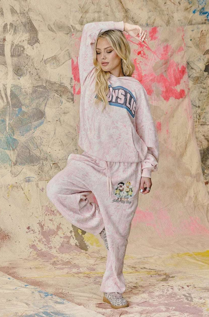 Woman in pink sweatshirt and pants posing against a textured wall with abstract designs.