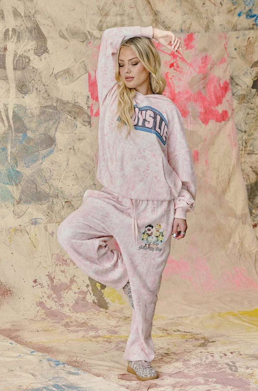 Woman in pink sweatshirt and pants posing against a textured wall with abstract designs.