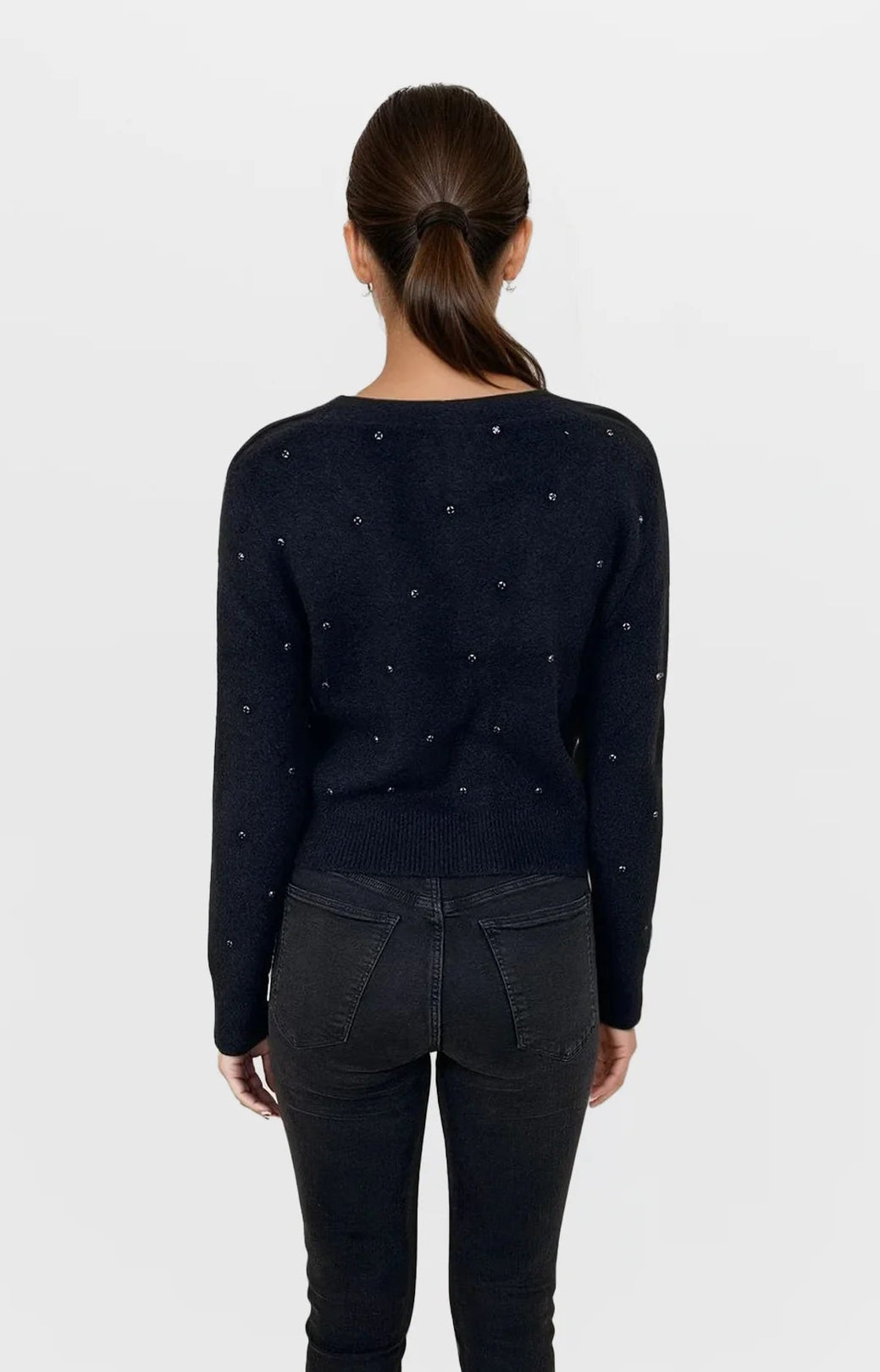 Person wearing a black sweater with small patterns and black pants on a white background