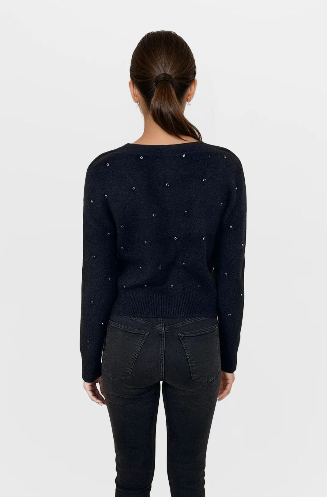 Person wearing a black sweater with small patterns and black pants on a white background