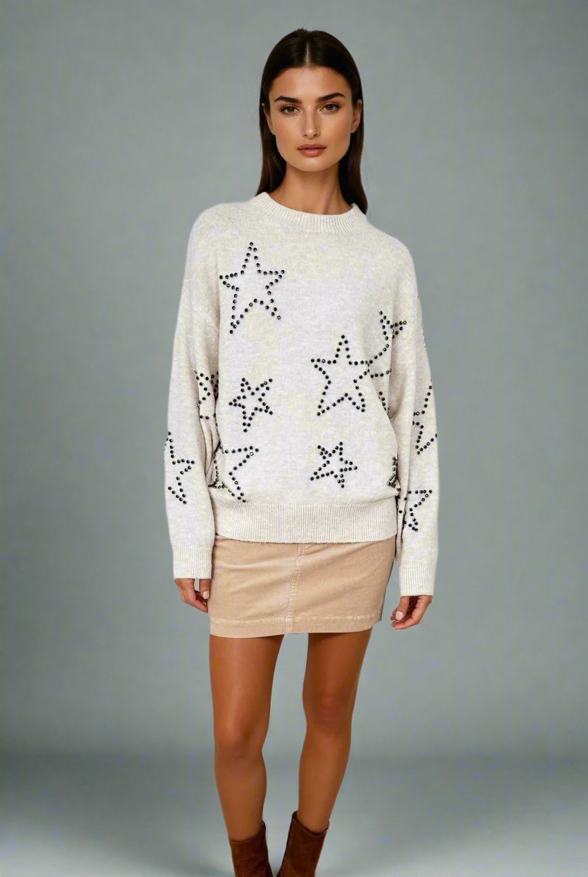 Woman wearing a cream sweater with star patterns on a white background