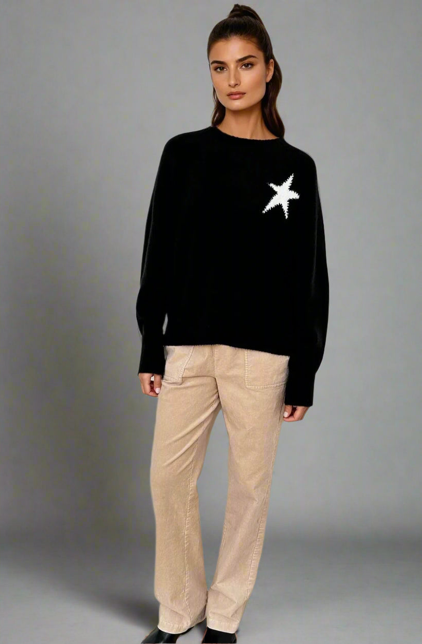 Woman wearing a black sweater with a white star design and beige pants on a white background