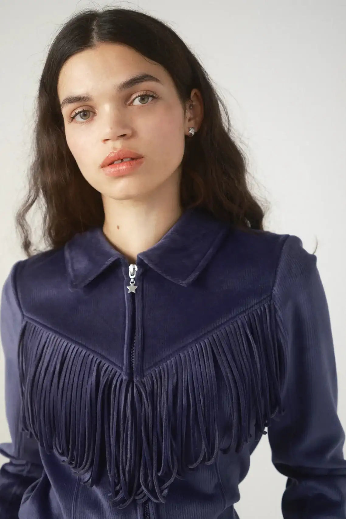Woman wearing a dark blue fringed jacket against a plain background
