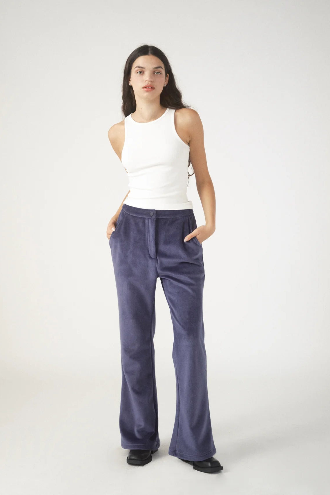 Woman wearing a white sleeveless top and blue pants on a white background