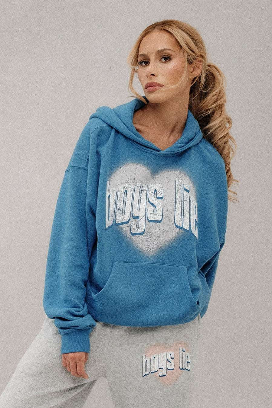 Woman wearing a blue hoodie with 'boys life' text, standing against a plain background