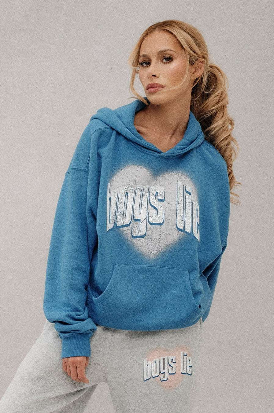 Woman wearing a blue hoodie with 'boys life' text, standing against a plain background