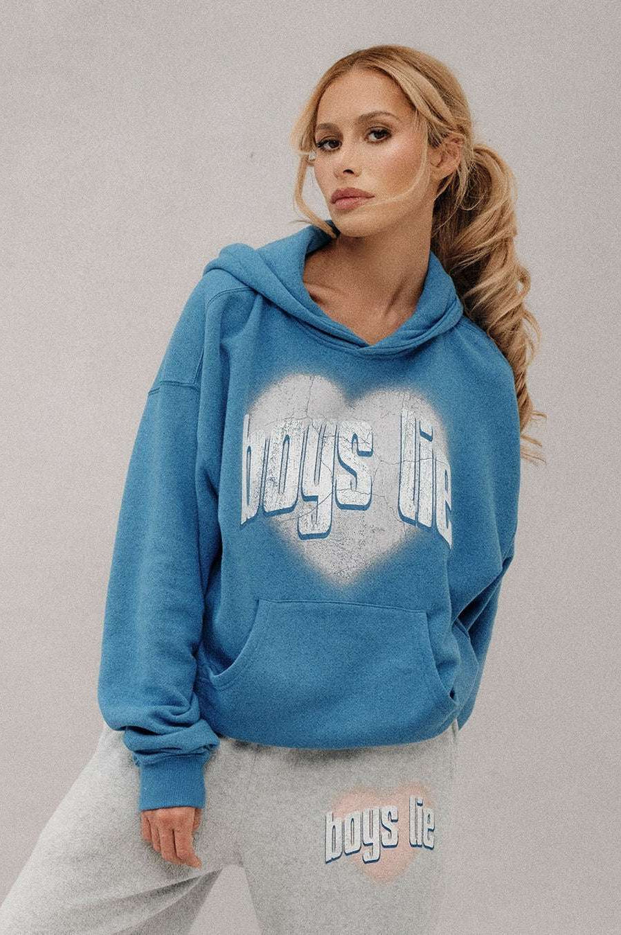 Woman wearing a blue hoodie with 'boys life' text, standing against a plain background
