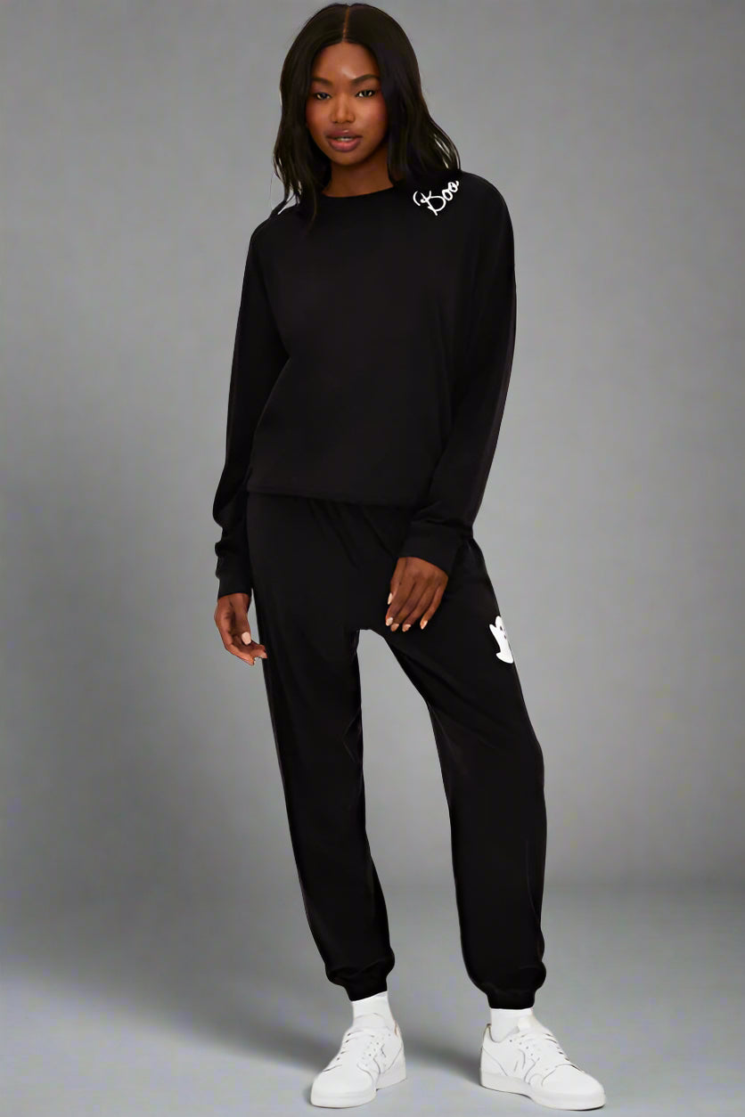 Person wearing a black tracksuit with brand logos on a white background