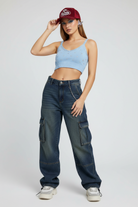 Woman wearing a light blue crop top, dark blue cargo pants, and a red cap on a white background