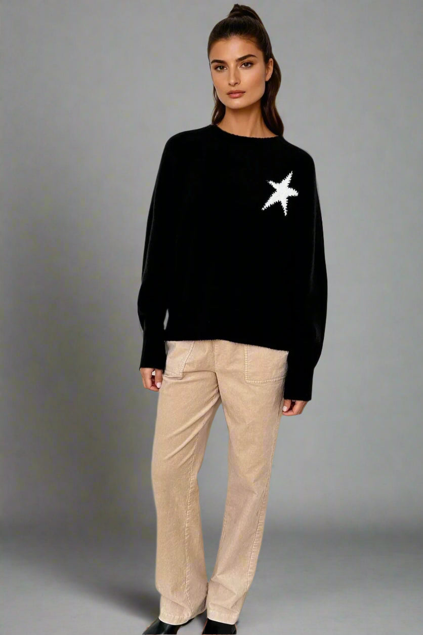 Woman wearing a black sweater with a white star design and beige pants on a white background