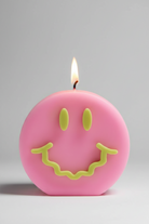 Pink candle with a smiley face design and a lit wick on a gray background