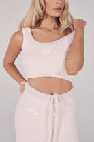 Woman wearing a light pink textured top and pants against a plain background