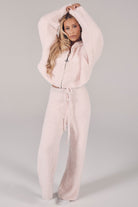 Woman wearing a light pink fleece tracksuit on a plain background